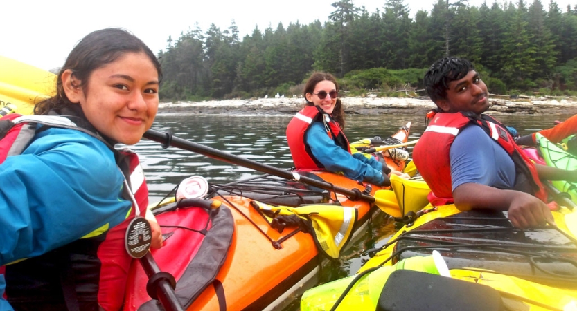 Students wearing life jackets smile from inside colorful kayaks